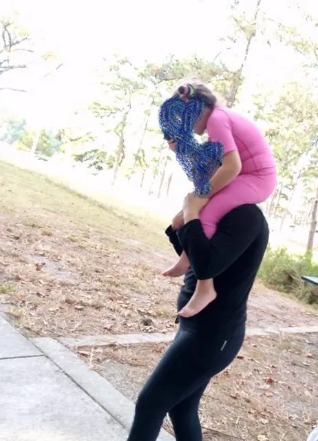Pembe SensoryRuns giysisiyle yetişkinin omzunda açık havada hareket eden çocuk